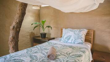 A bedroom with a canopy bed, a potted plant, and a tree trunk against the wall.