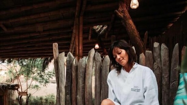 A person sitting in a hot tub with floral petals floating on the water, surrounded by wooden structures and greenery. - AguaMar Vichayito (Los Organos)
