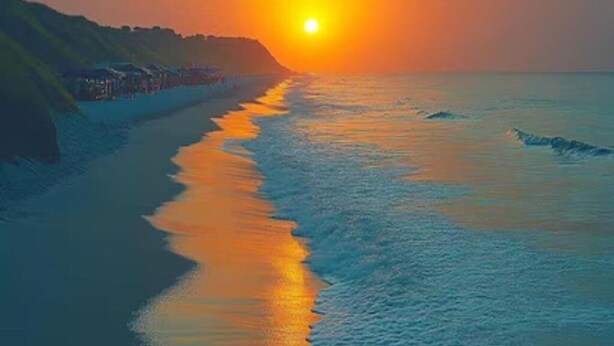 A beach with a sunset over the ocean, a coastline with buildings, and waves approaching the shore. - Pepper Jazz Varkala : Double Room with Private Bathroom (Varkala)