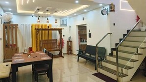 A modern living room with a dining area, a staircase, and a kitchen in the background. - Pepper Jazz Varkala : Double Room with Private Bathroom (Varkala)