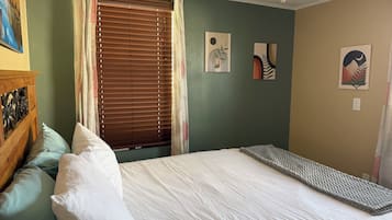 A bedroom with a bed, pillows, a headboard, a window with blinds, and wall art.