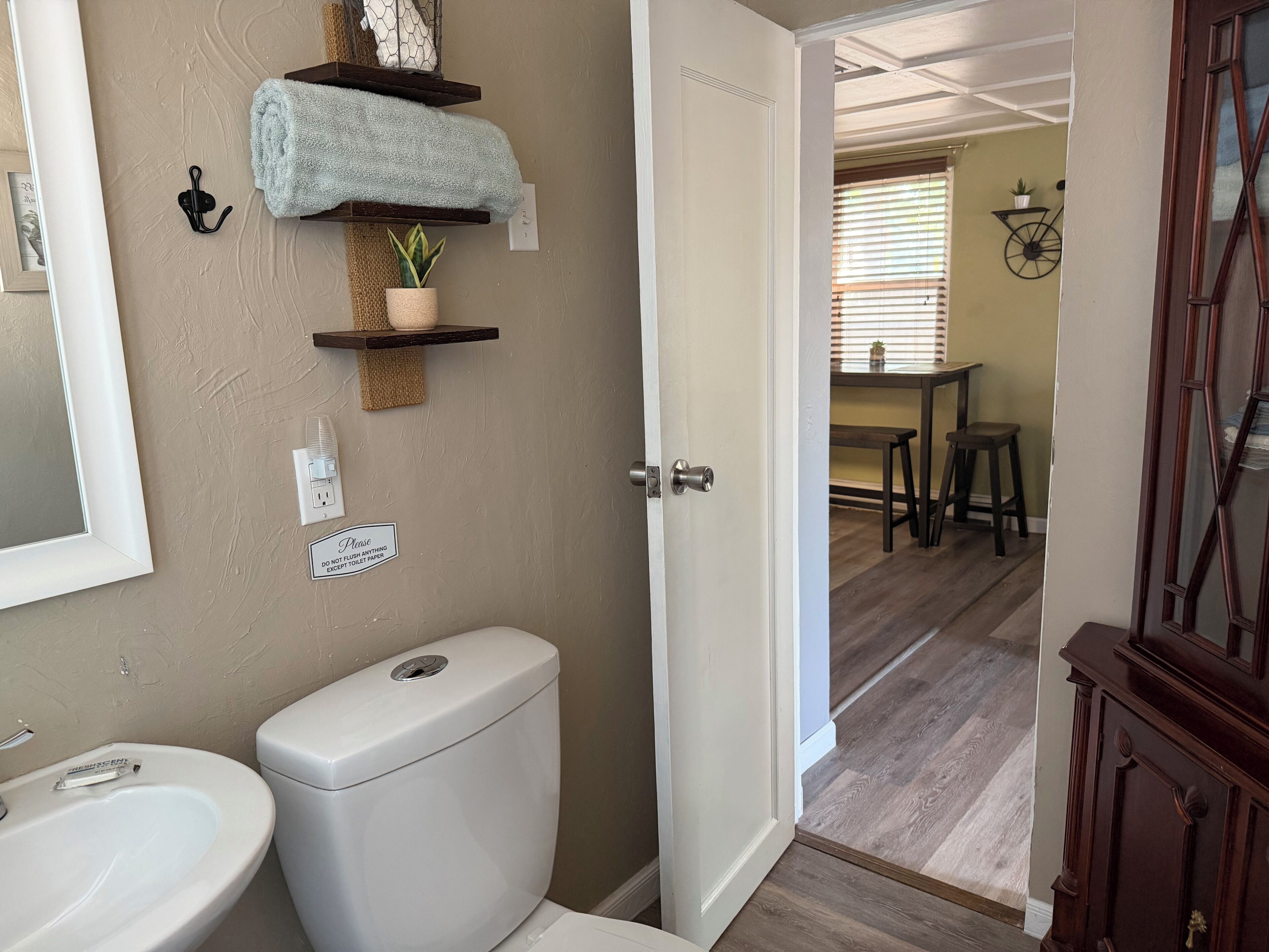 A bathroom with a toilet, sink, towel rack, and a sign requesting no toilet paper.