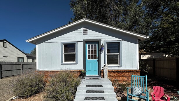 Una casa a un piano con una porta blu, un tappetino d'ingresso e un piccolo portico con due sedie.