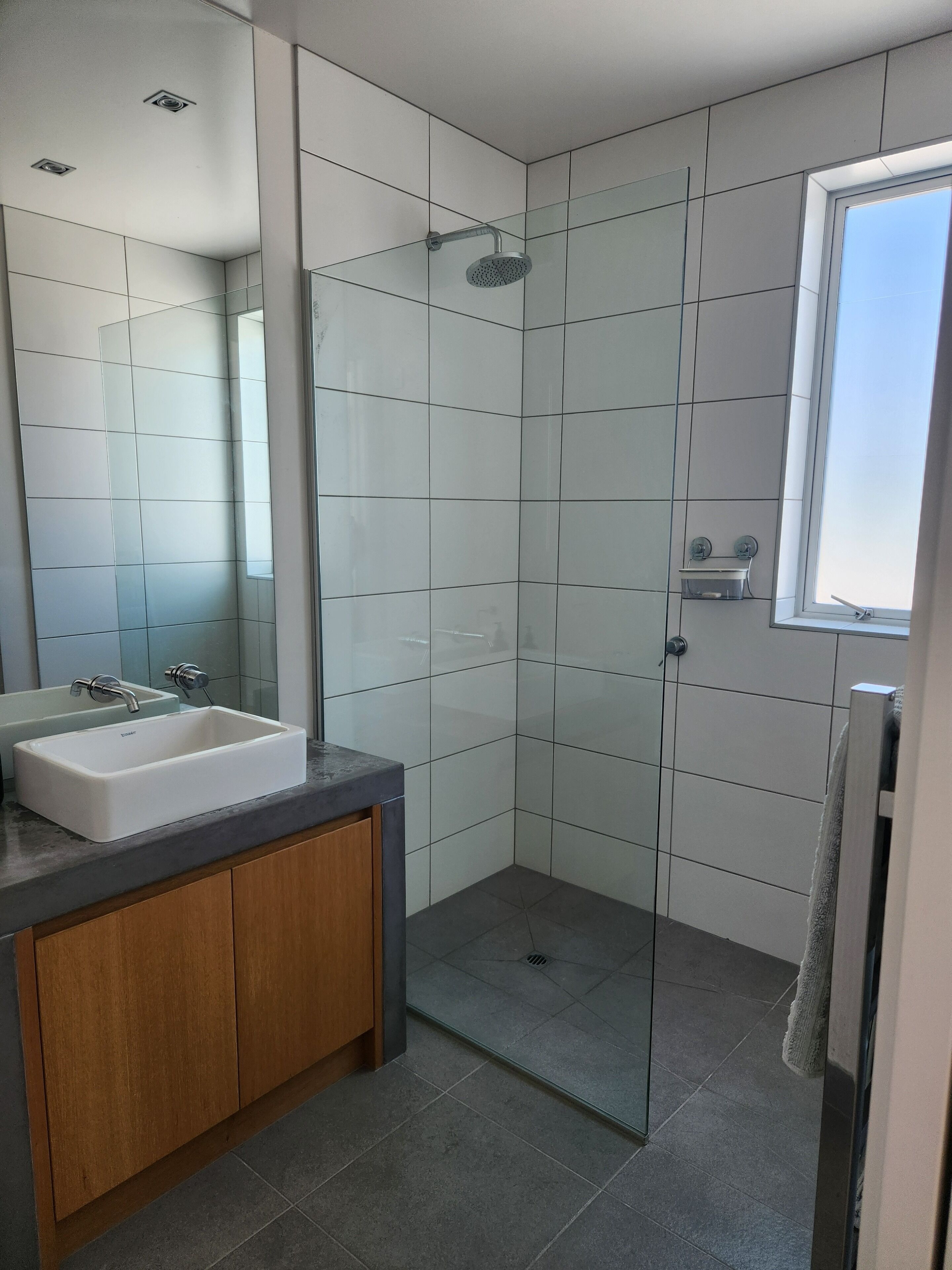 Un baño moderno con cabina de ducha de vidrio, lavabo con mueble de madera y un espejo grande.