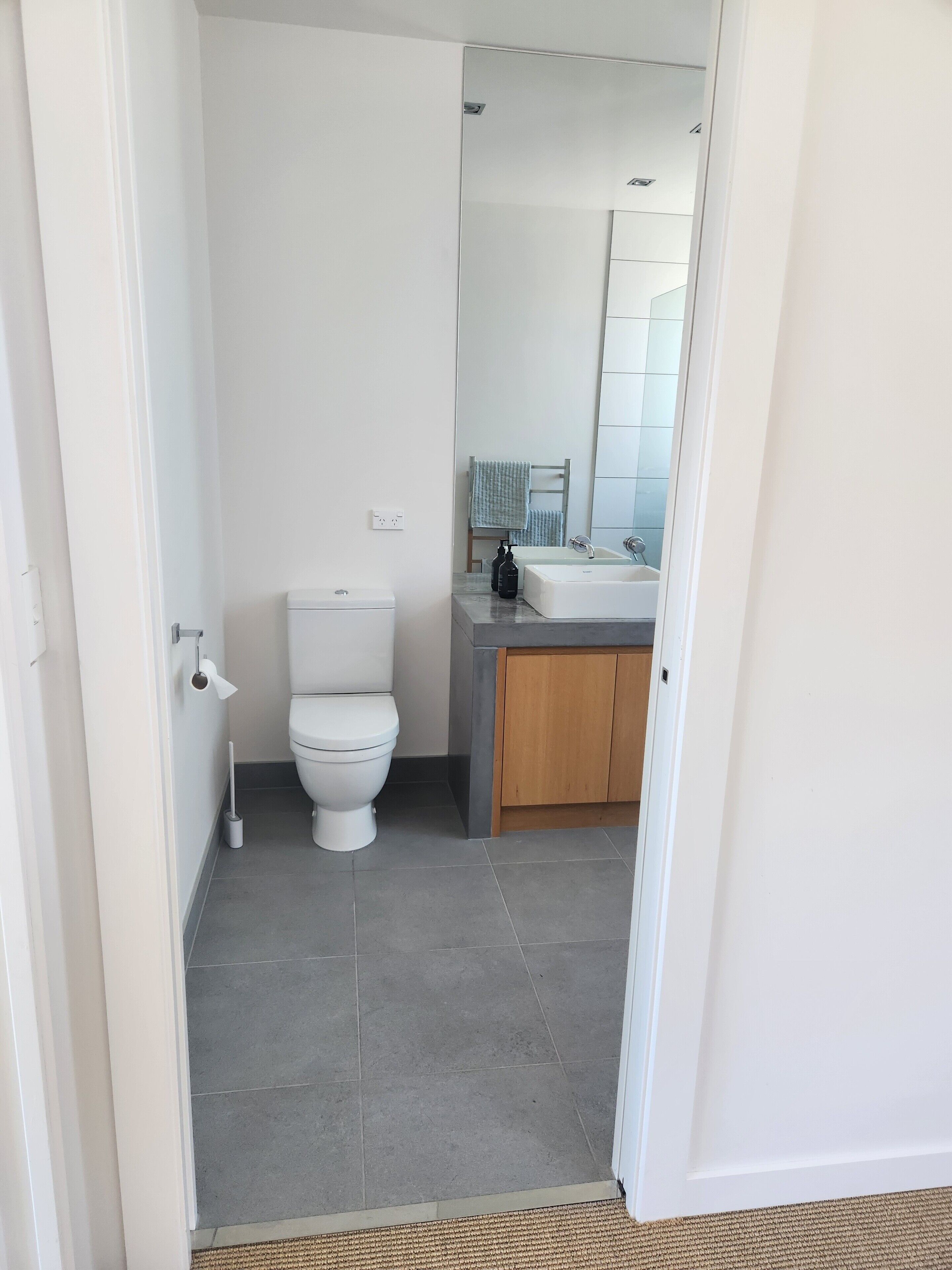 Een moderne badkamer met toilet, wastafel en spiegel.