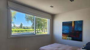 A bedroom with a large window, a bed, and a colorful abstract painting on the wall. - Vineyard accommodation close to Renwick. Quiet apartment surrounded by vines. (Hawkesbury)