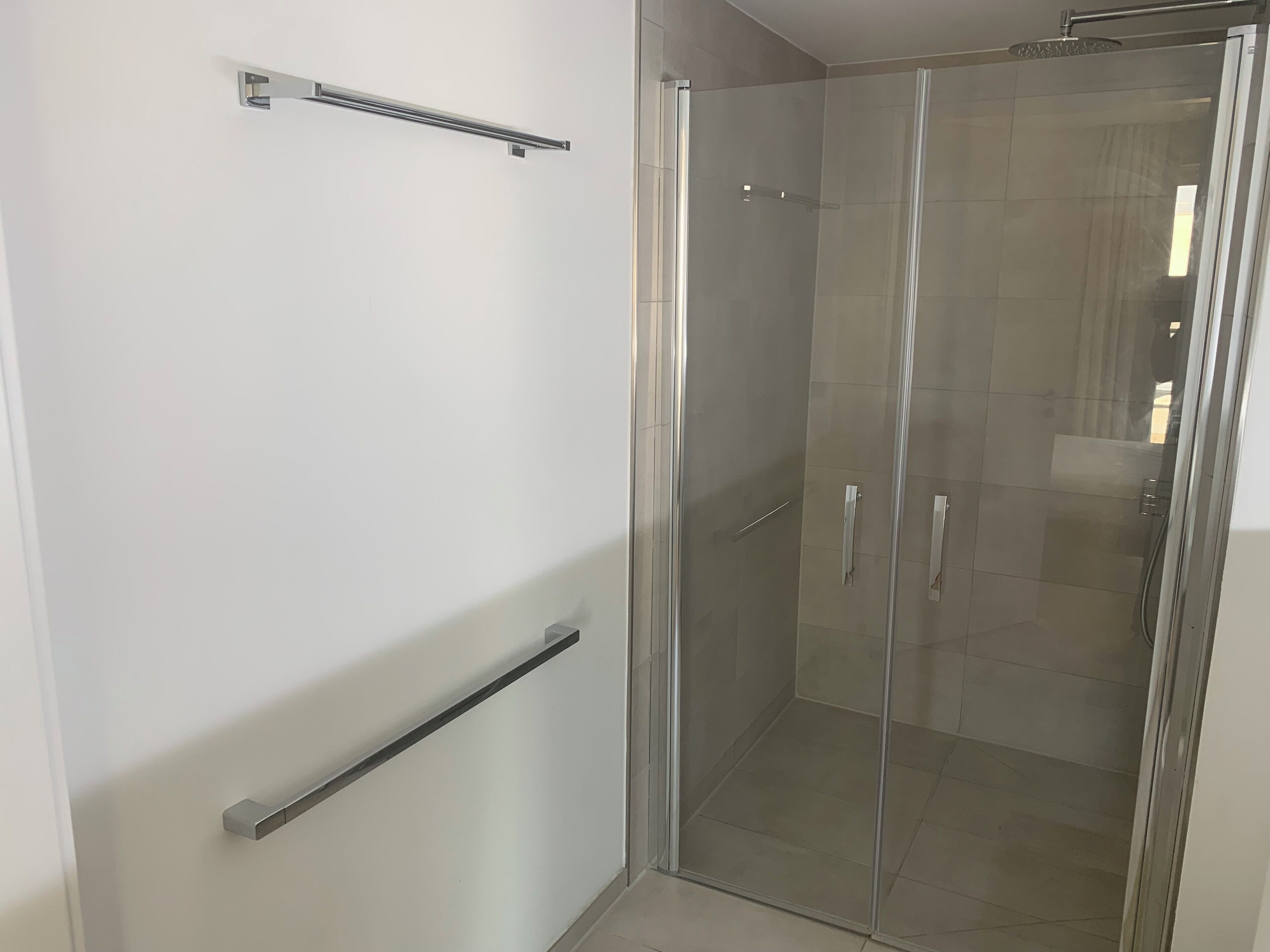 A modern bathroom with a glass shower enclosure, a towel rack, and a handrail.