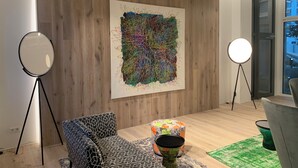 Una galería de arte moderno con piso de madera, una pintura abstracta de gran tamaño y dos trípodes con luces.