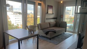 Una sala de estar moderna con un sofá, una mesa de comedor y vistas de la ciudad a través de amplios ventanales.