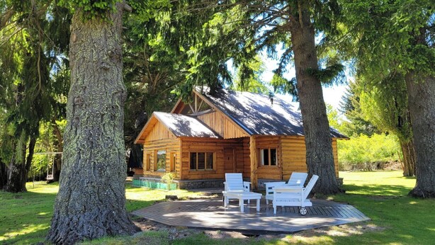 A wooden cabin with a deck and two lounge chairs.