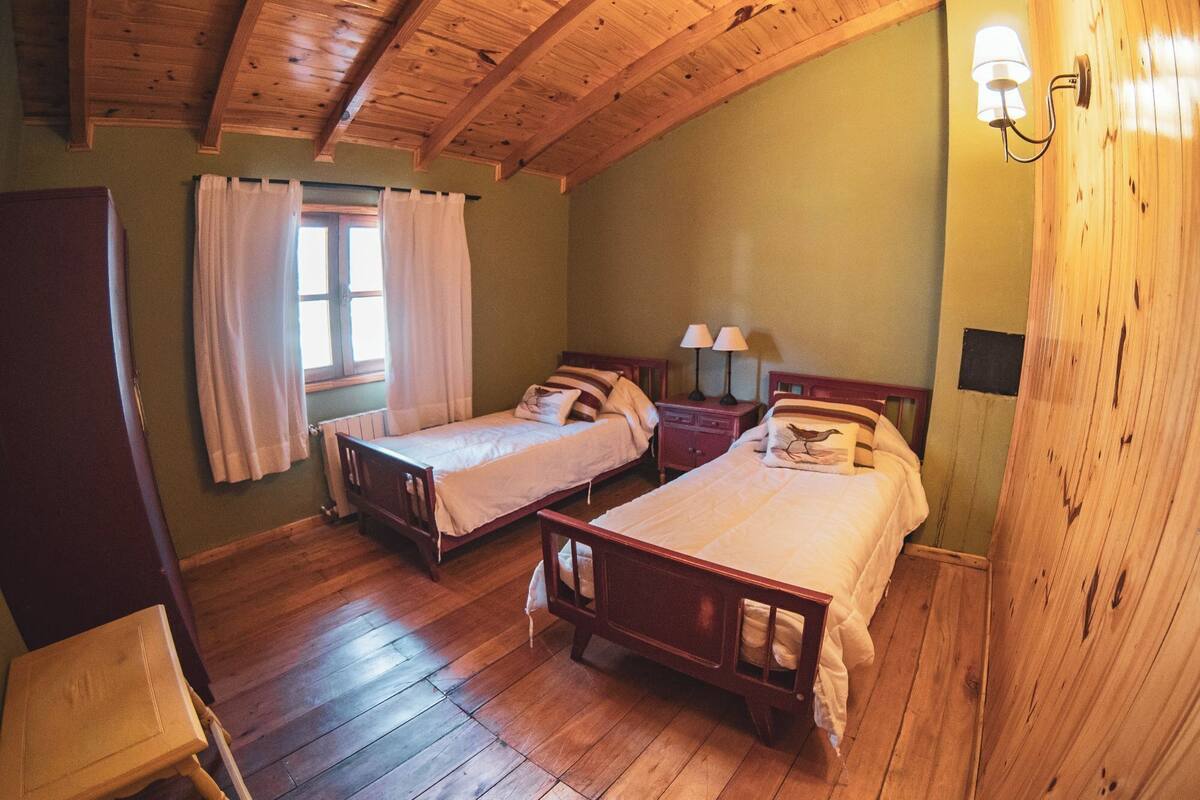 Een kamer met twee houten bedden, een raam met gordijnen en een wandlamp.