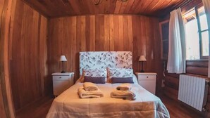 A wooden-paneled bedroom with a bed, two bedside tables, and a window with curtains.