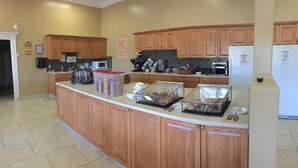 A kitchen with wooden cabinets, a coffee station, and a refrigerator. - New Imperial Suites (Whitecourt)
