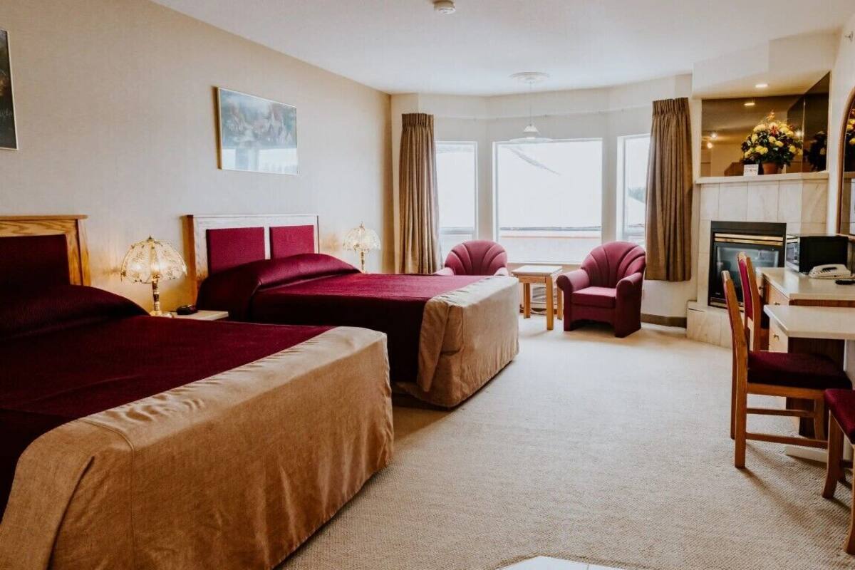 Une chambre d’hôtel avec deux lits, un bureau, une chaise, une cheminée et une grande fenêtre.