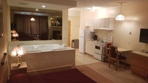 A compact hotel room with a kitchenette, a dining area, and a large mirror reflecting the living room. - New Imperial Suites (Whitecourt)