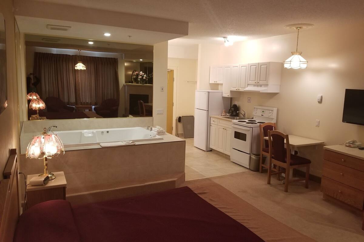 Une chambre d’hôtel compacte dotée d’une kitchenette, d’un coin repas et d’un grand miroir qui reflète le salon.