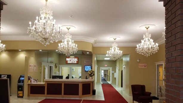A hotel reception area with a red carpet, a reception desk, and chandeliers. - New Imperial Suites (Whitecourt)