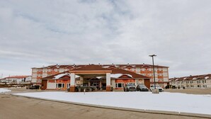 A multi-story hotel with a central entrance and a covered parking area. - New Imperial Suites (Whitecourt)