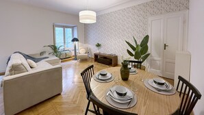 En matplats med ett runt bord för fyra personer, omgivet av stolar. I bakgrunden finns en soffa, en krukväxt på bordet och ett fönster med utsikt över omgivningen.