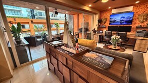 A modern living room with a sofa, coffee table, and a TV. There is a balcony with plants and a view of buildings. - Paradise Escape, Life is Good! (Puerto Vallarta)