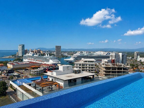 A hotel with a swimming pool, a view of the city, and cruise ships in the background.