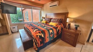A bedroom with a bed, a TV mounted on the wall, a window, a bedside table, and a lamp. - Paradise Escape, Life is Good! (Puerto Vallarta)