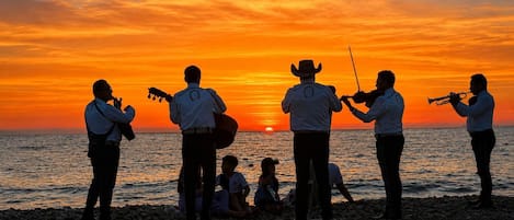 A group of people playing musical instruments on a beach at sunset.