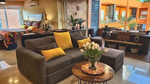 A living room with a brown sofa, yellow cushions, a coffee table with a vase of flowers, and a colorful rug. - Paradise Escape, Life is Good! (Puerto Vallarta)