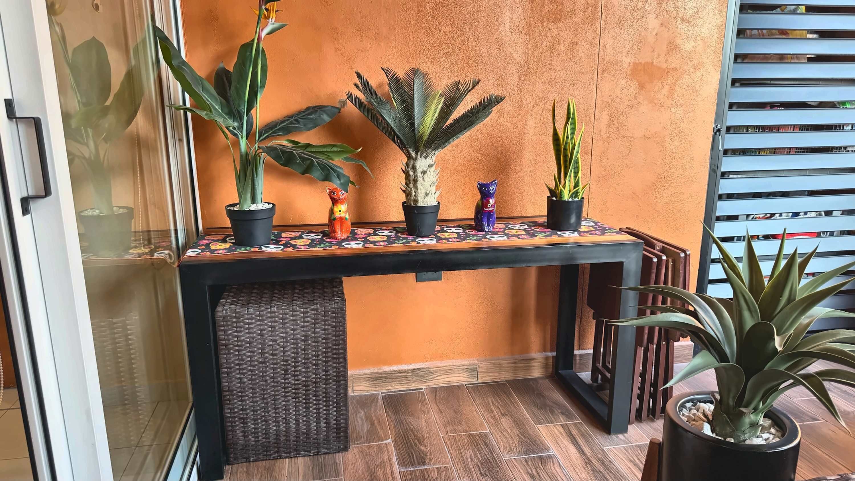 A balcony with a table, potted plants, and a decorative cat statue.