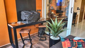 A small office space with a desk, a chair, a potted plant, and a glass door leading to a hallway.