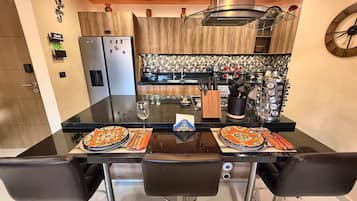 A modern kitchen with a central island, two refrigerators, a sink, and a clock on the wall.
