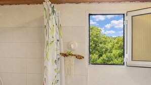 A bathroom with a shower curtain featuring a leaf pattern, a window with a view of greenery, and a towel rack with a decorative item. - Casa Di Babbo (Olmi-Cappella)