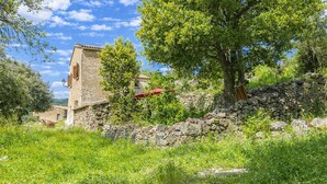 A rustic stone building with a red roof, surrounded by lush greenery and a stone wall. - Casa Di Babbo (Olmi-Cappella)