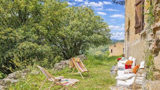 An outdoor seating area with two wooden chairs, a stone wall, and a rustic building in the background. - Casa Di Babbo (Olmi-Cappella)