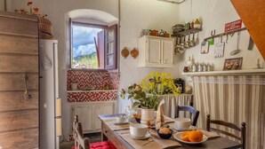 A rustic kitchen with a wooden cabinet, a window with an open door, and a table set with dishes and a vase of flowers. - Casa Di Babbo (Olmi-Cappella)