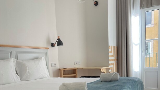 A neatly made bed with a blue blanket, a bedside lamp, and a wooden nightstand. - Bacalhoeiros 125 Hotel (Lisbon)