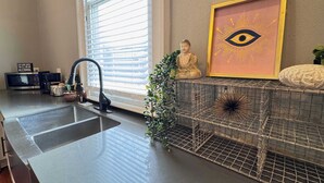 A kitchen with a sink, a Buddha statue, a framed eye symbol, and a wire basket.