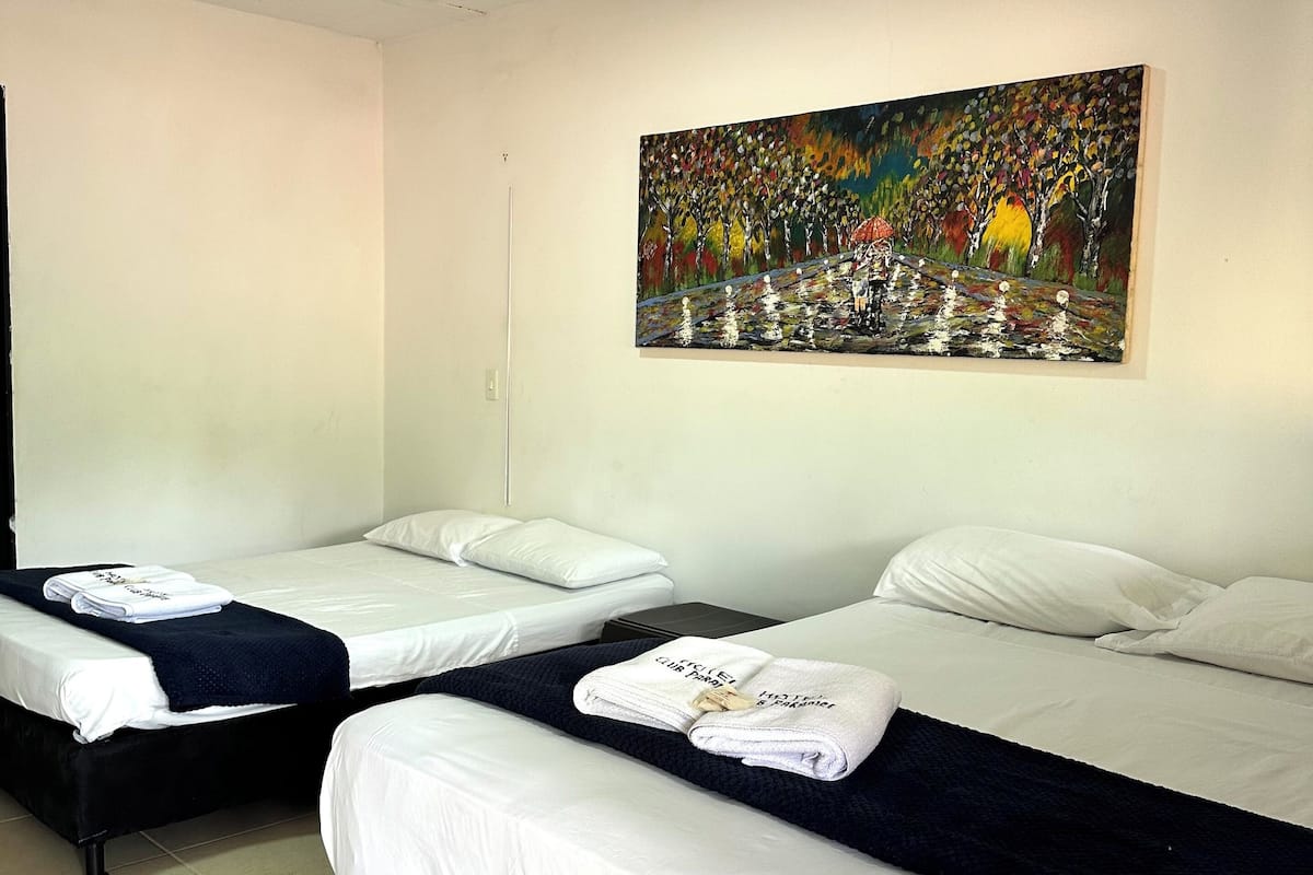 Habitació d'hotel amb dos llits, roba de llit blanca, un quadre a la paret i una làmpada al sostre.