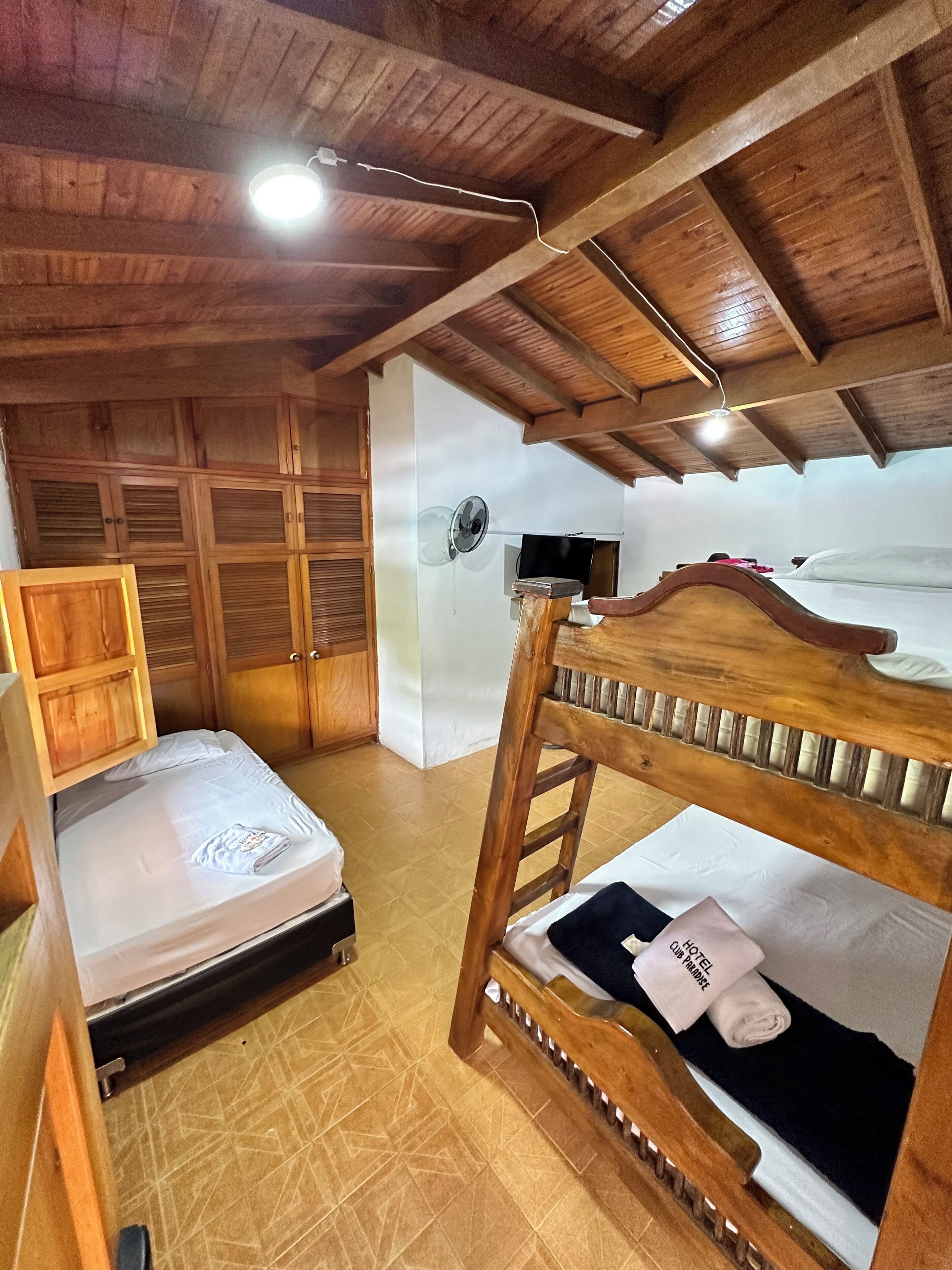 A rustic wooden room with bunk beds, a wooden wardrobe, and a ceiling fan.
