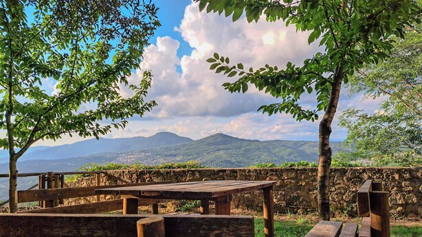 Uma área de estar ao ar livre rústica, com bancos e mesas de madeira, com vista para uma paisagem montanhosa.