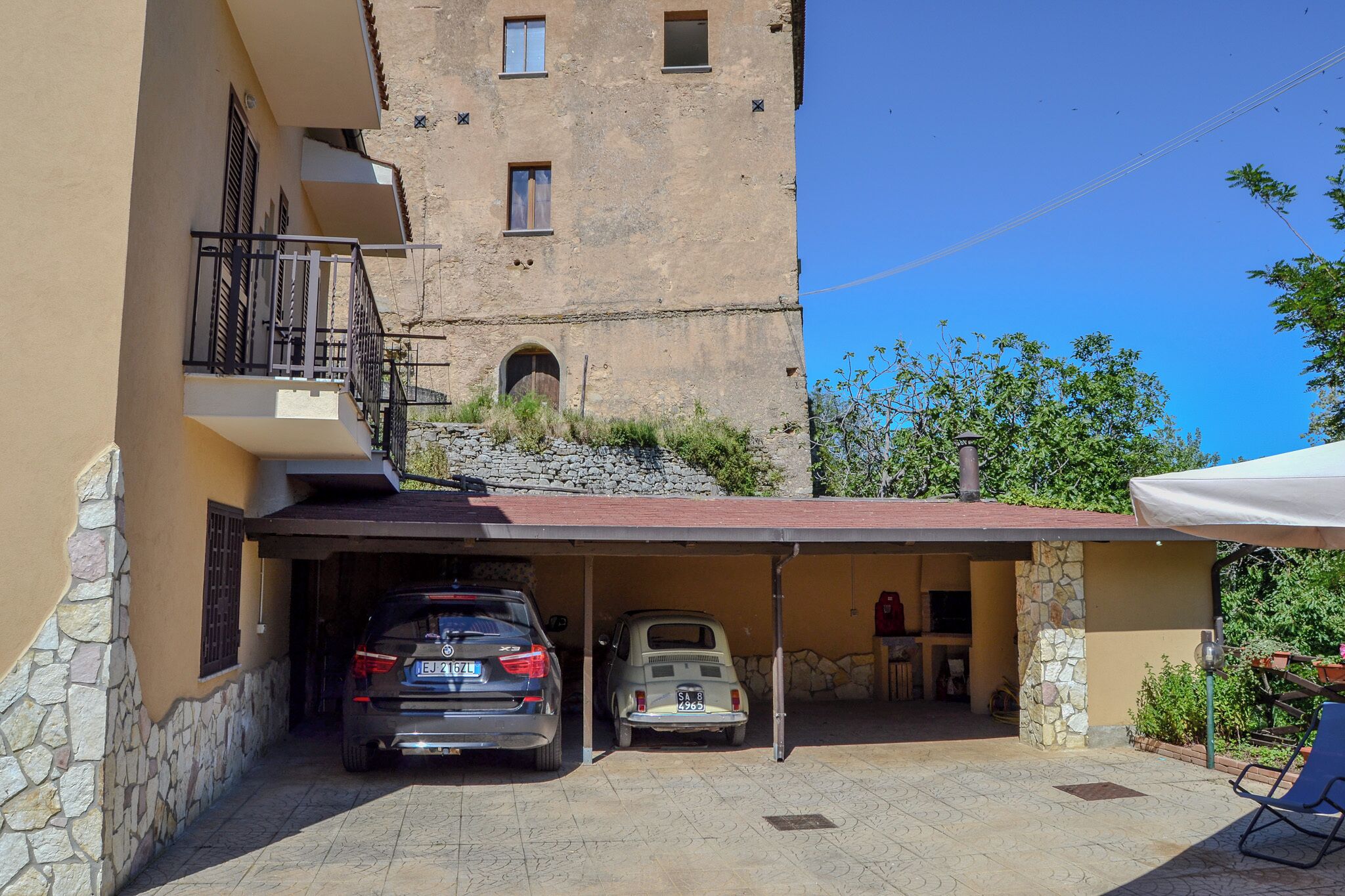 Un edificio con fachada de piedra, una zona de estacionamiento techada y un pequeño espacio al aire libre con una mesa y sillas.