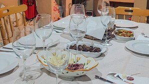 Mesa de jantar posta para refeição, com copos de vinho, pratos e diversos alimentos.