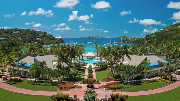 Un resort con piscina central, rodeado de palmeras y vistas al océano.