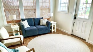 Un salon avec un canapé bleu, deux lampes blanches, un tapis rond et un plancher en bois.