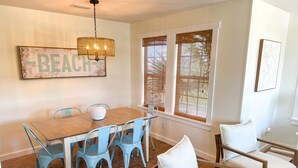 Un coin repas avec une table en bois et des chaises bleues, un lustre et un panneau indiquant « PLAGE » sur le mur.