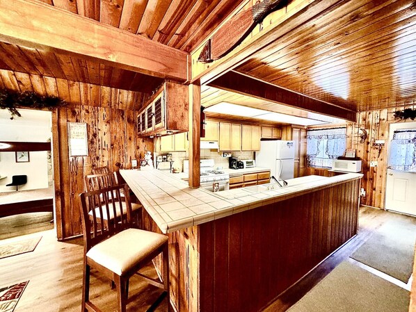 A rustic kitchen with wooden walls, a central island, and basic appliances.
