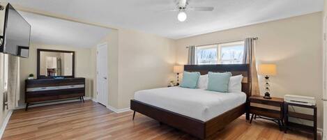 A bedroom with a large bed, a dresser, a TV, and a ceiling fan.