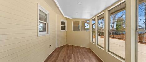 A hallway with wooden flooring, large windows, and a view of an outdoor area.
