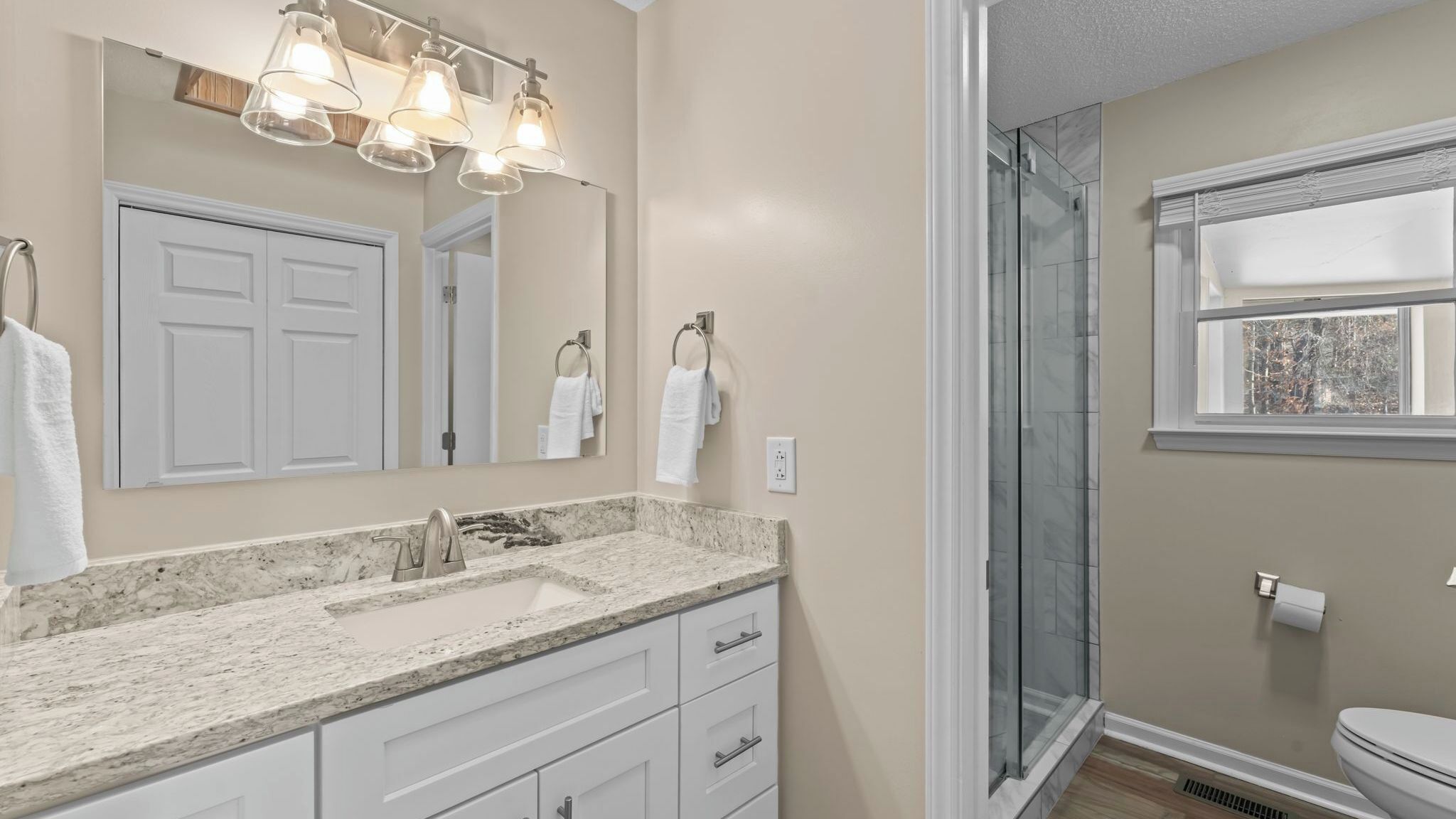 A bathroom with a marble sink, a glass shower enclosure, and a toilet.