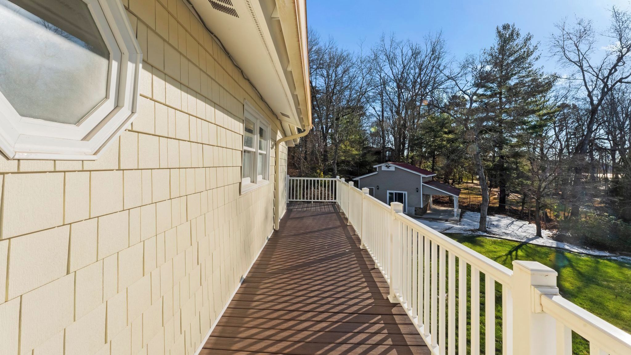 Una veranda in legno coperta con ringhiera bianca, che conduce a una casa con un piccolo garage annesso.
